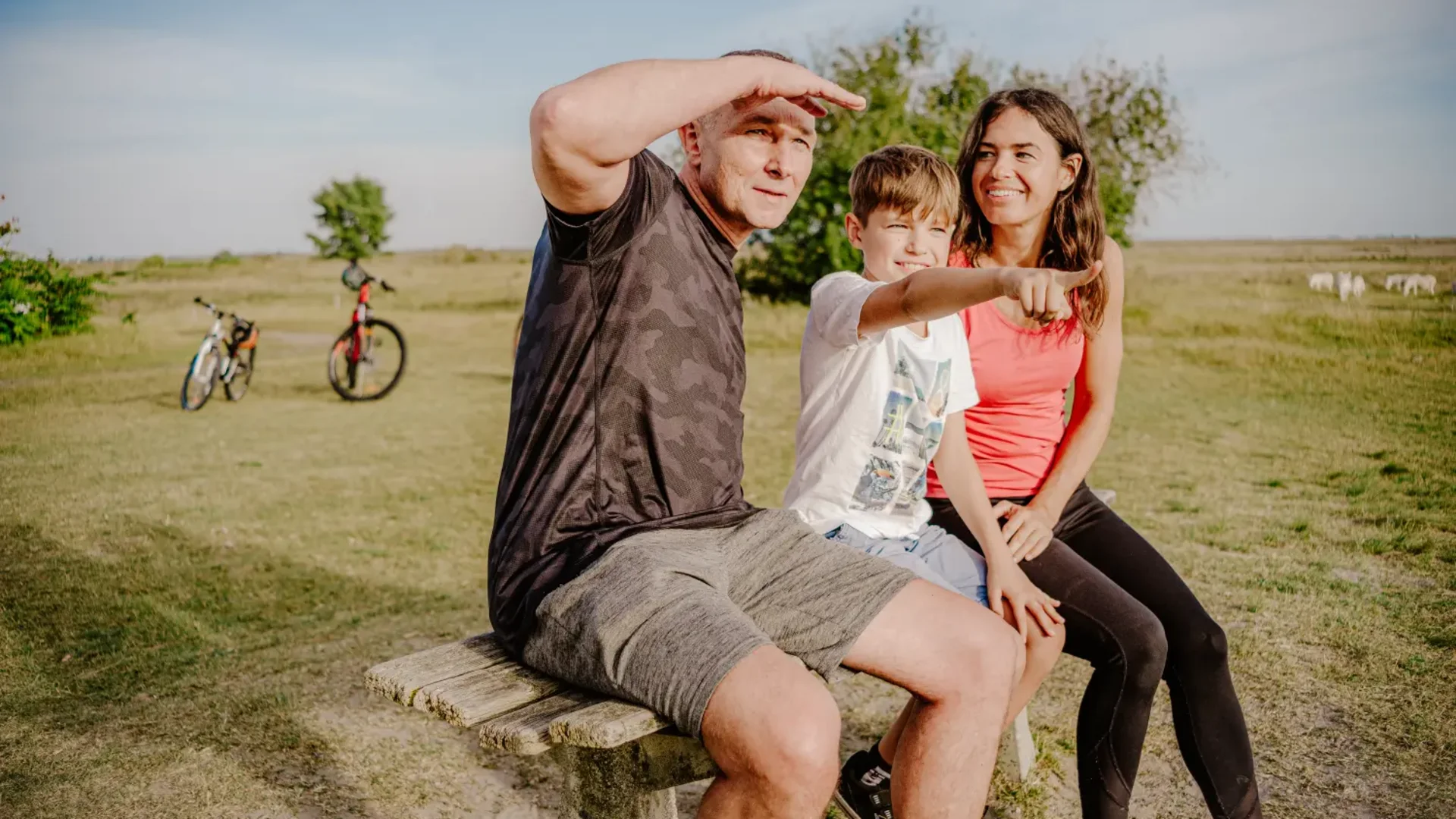 Familie sitzt auf Bank im Park mit Fahrrädern im Hintergrund