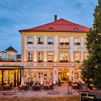 Abendansicht des Hotels Zur Post mit beleuchtetem Außenbereich und Gästen