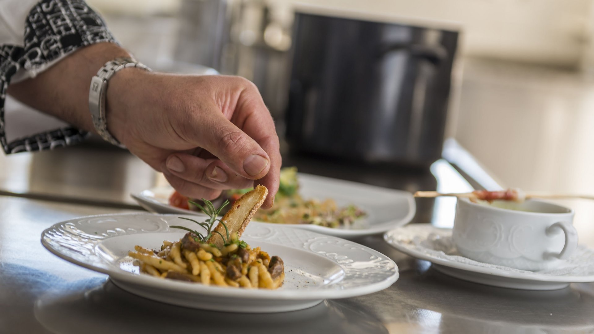 Hand garnishing pasta dish with bread on white plates