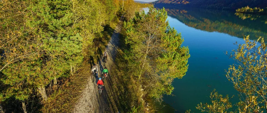 Radfahrer auf Waldweg neben ruhigem Fluss in herbstlicher Landschaft
