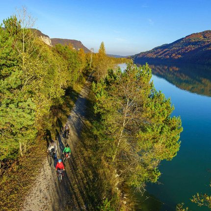 Cyclists on forest path next to calm river in autumn landscape