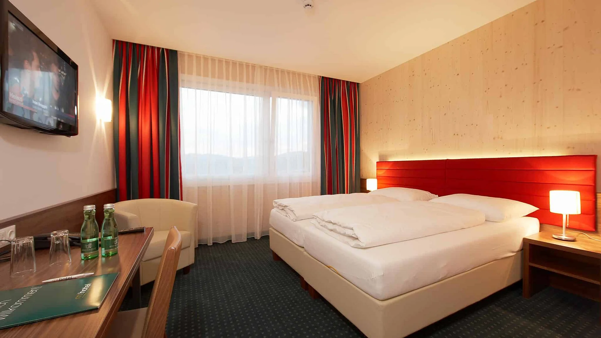 Moderne hotelkamer met tweepersoonsbed, rood hoofdeinde en bureau