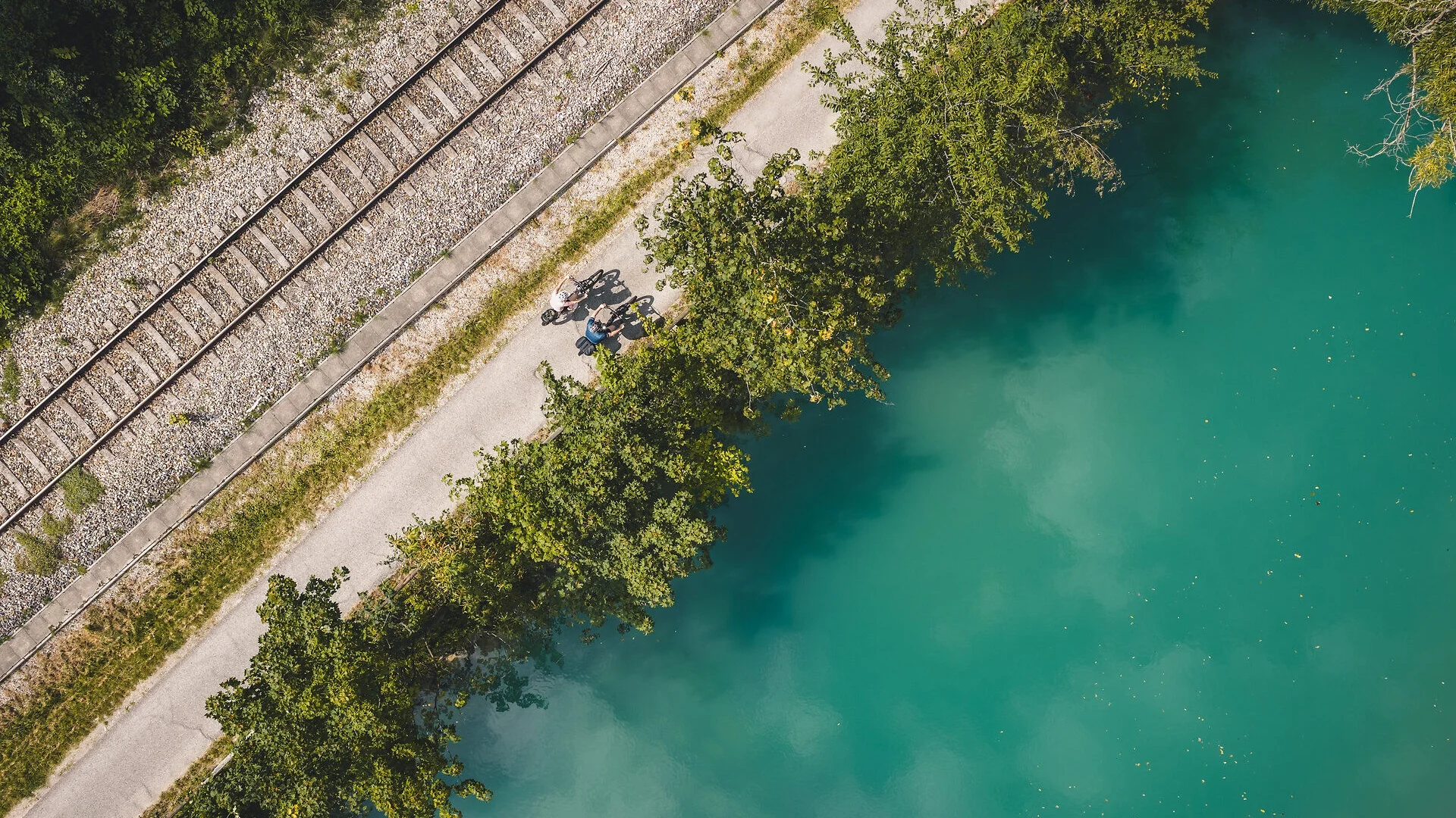 Tour-Detail Zwei Radfahrer auf Weg neben Bahngleisen und blauem Wasser