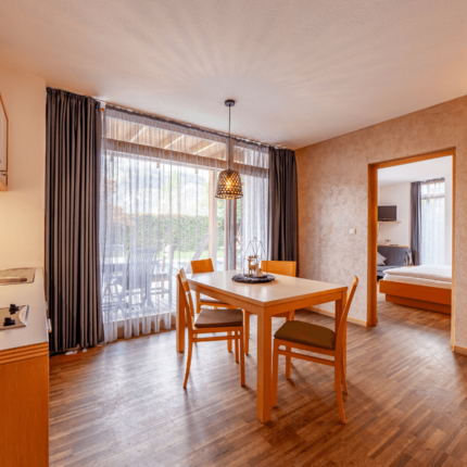 Dining area with wooden table, chairs, kitchenette, and view into bedroom
