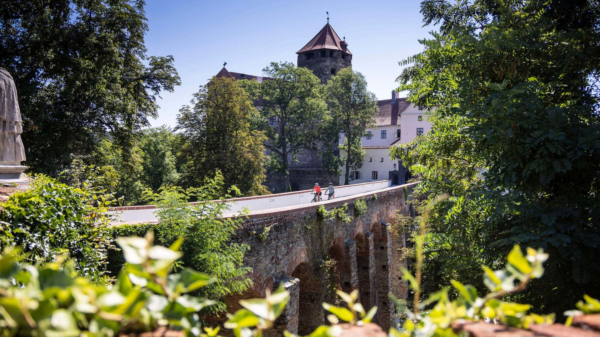 Old stone bridge with two cyclists near a castle and trees