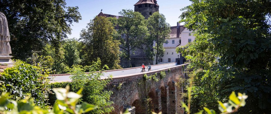Old stone bridge with two cyclists near a castle and trees