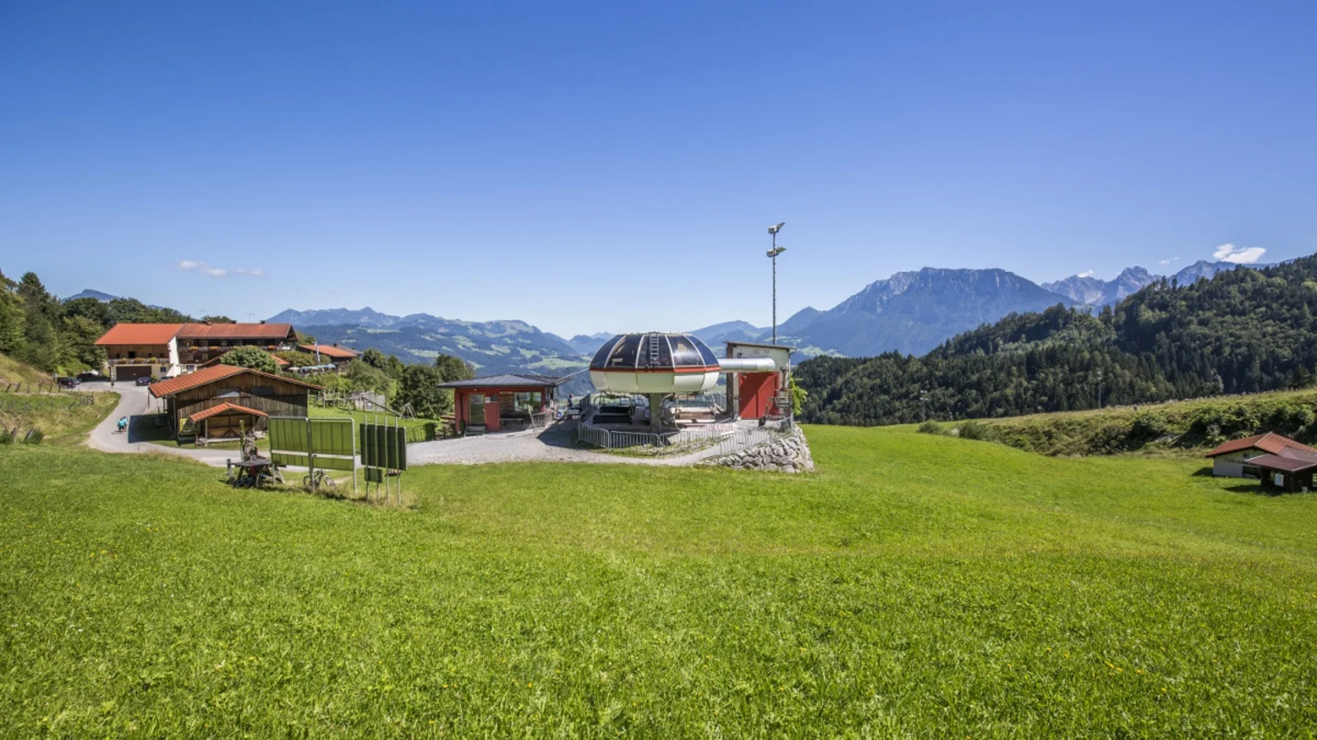 Grünes Tal mit Alpen und Skiliftstation unter blauem Himmel