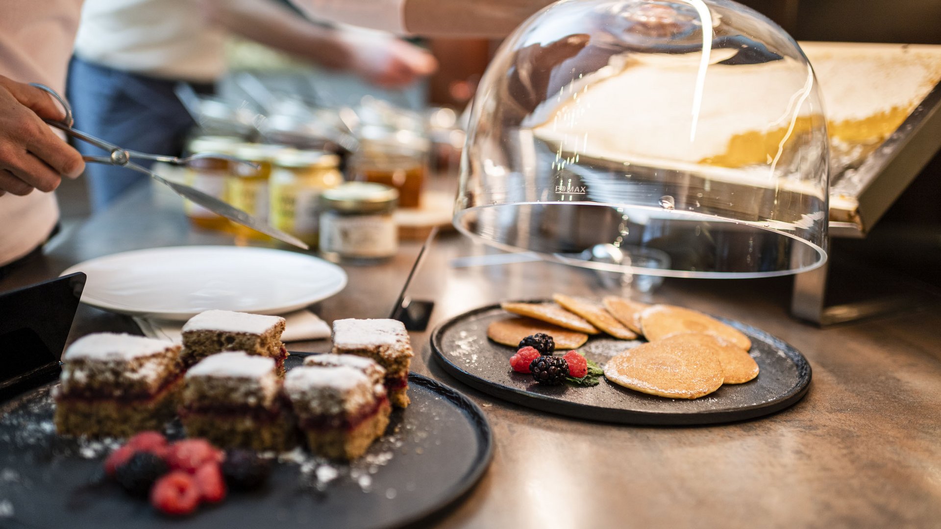 Various cake slices and pancakes with berries on black plates