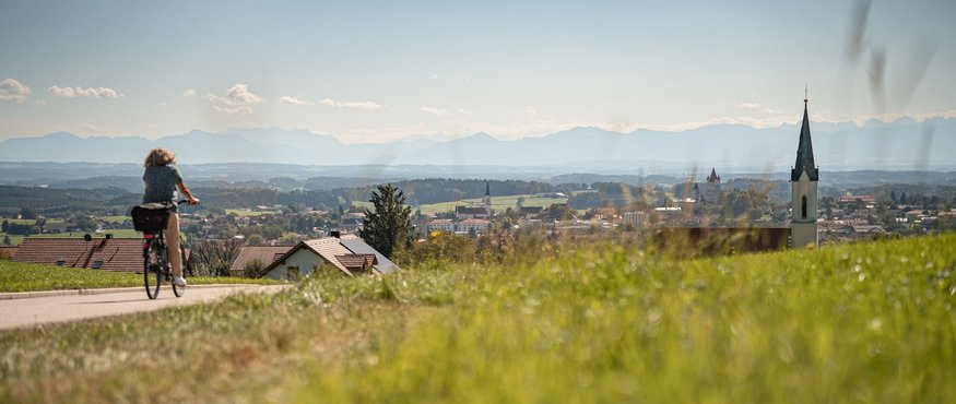 Cyclist on country road with village and mountain view