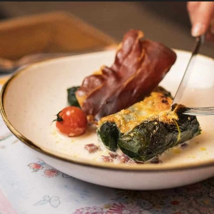 Person eating stuffed chard rolls with ham and tomato using fork and knife