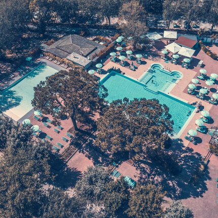 Aerial view of outdoor swimming pools with umbrellas and surrounding trees