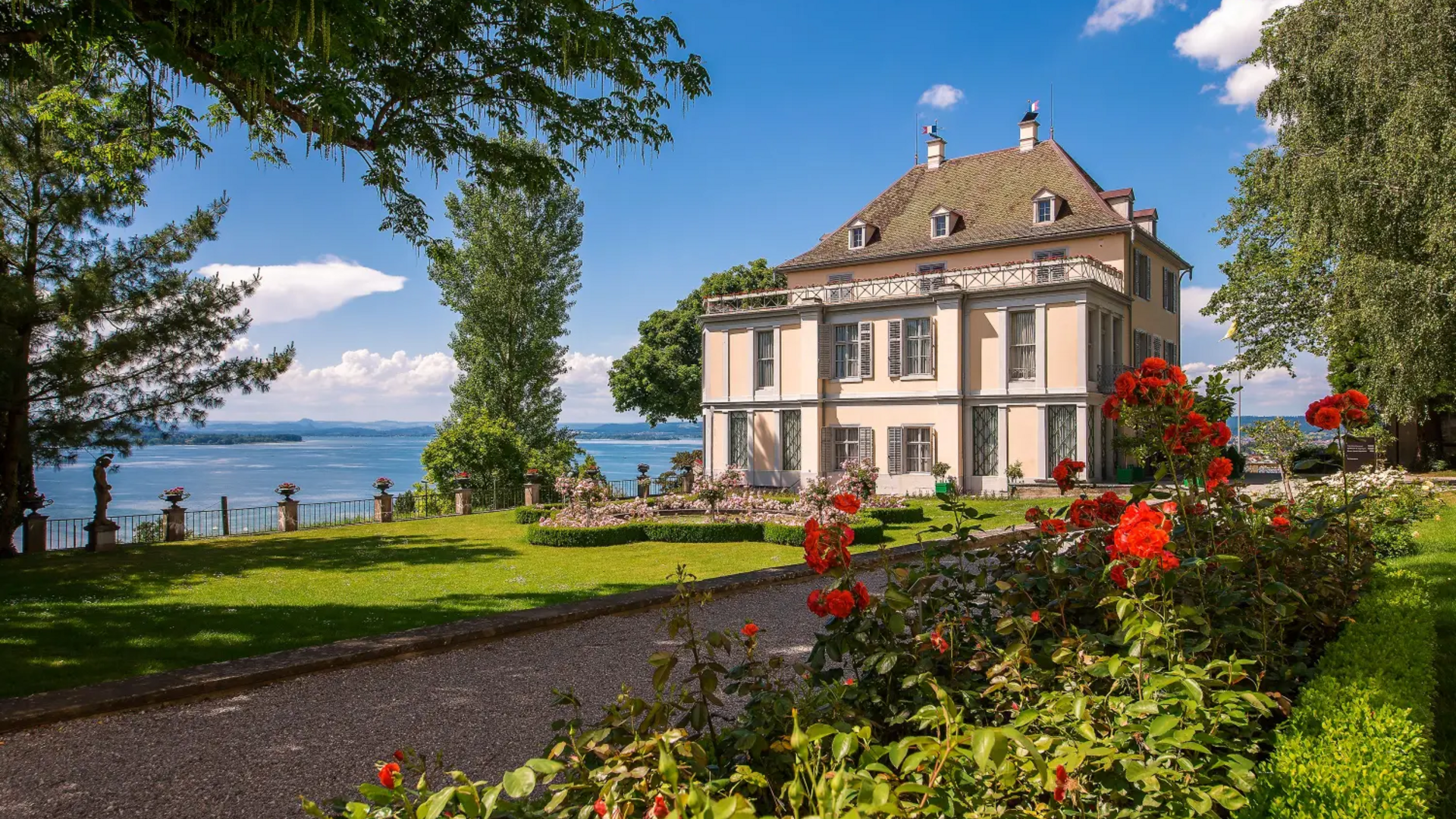House with garden and red flower bed by lake on sunny day