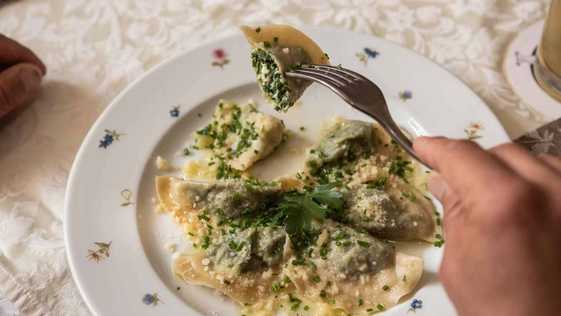 Bord met spinazie ravioli en kaas, persoon houdt ravioli met vork vast