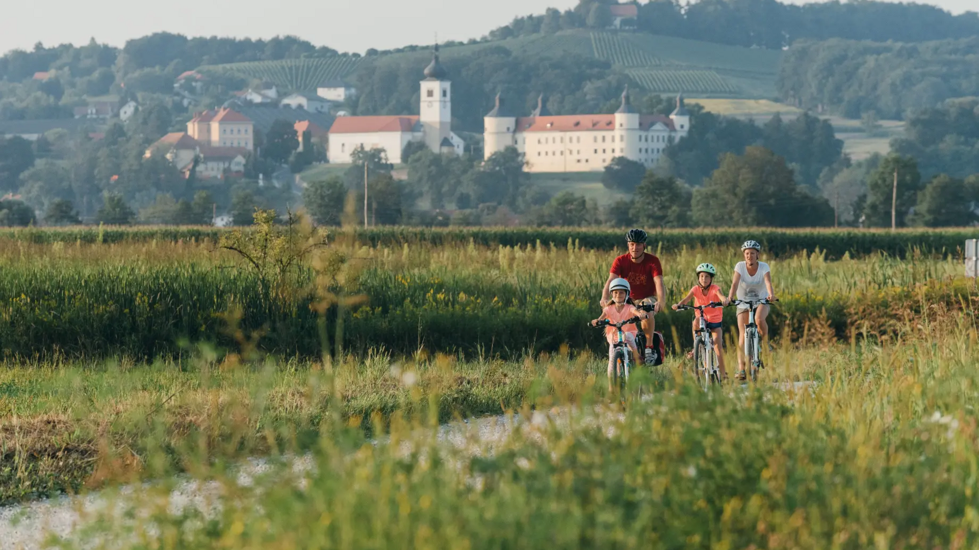Family cycling on a path through green fields with a castle in the background