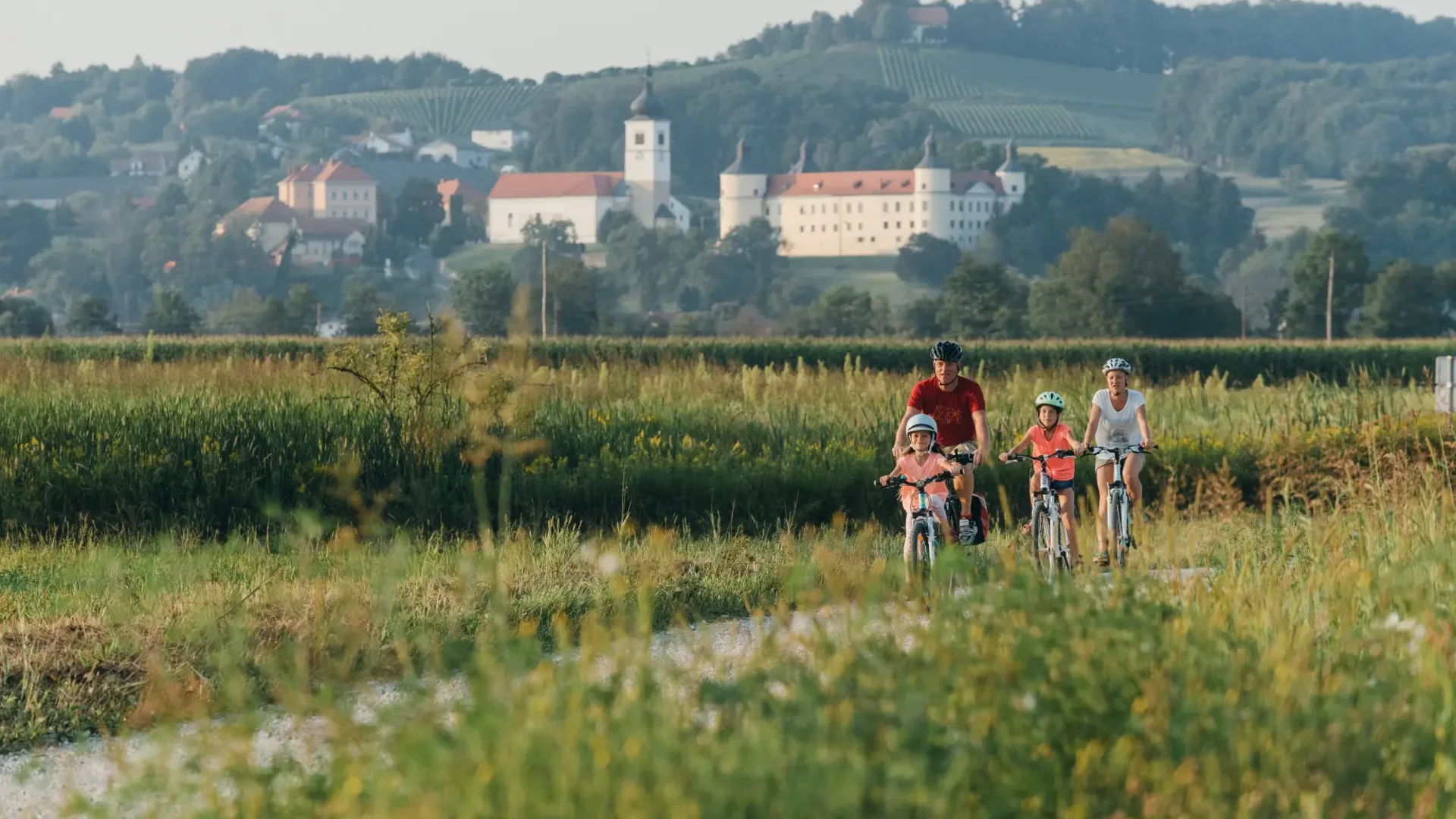 Familie fietst op een pad door groene velden met kasteel op de achtergrond
