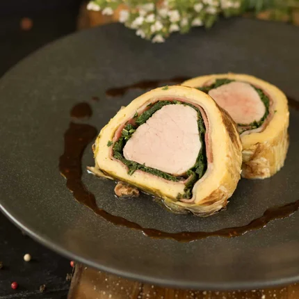 Twee plakjes gevulde vleesschotel op een zwart bord met saus