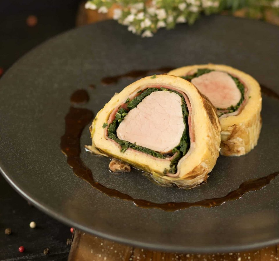 Two slices of stuffed meat dish served on a black plate with sauce