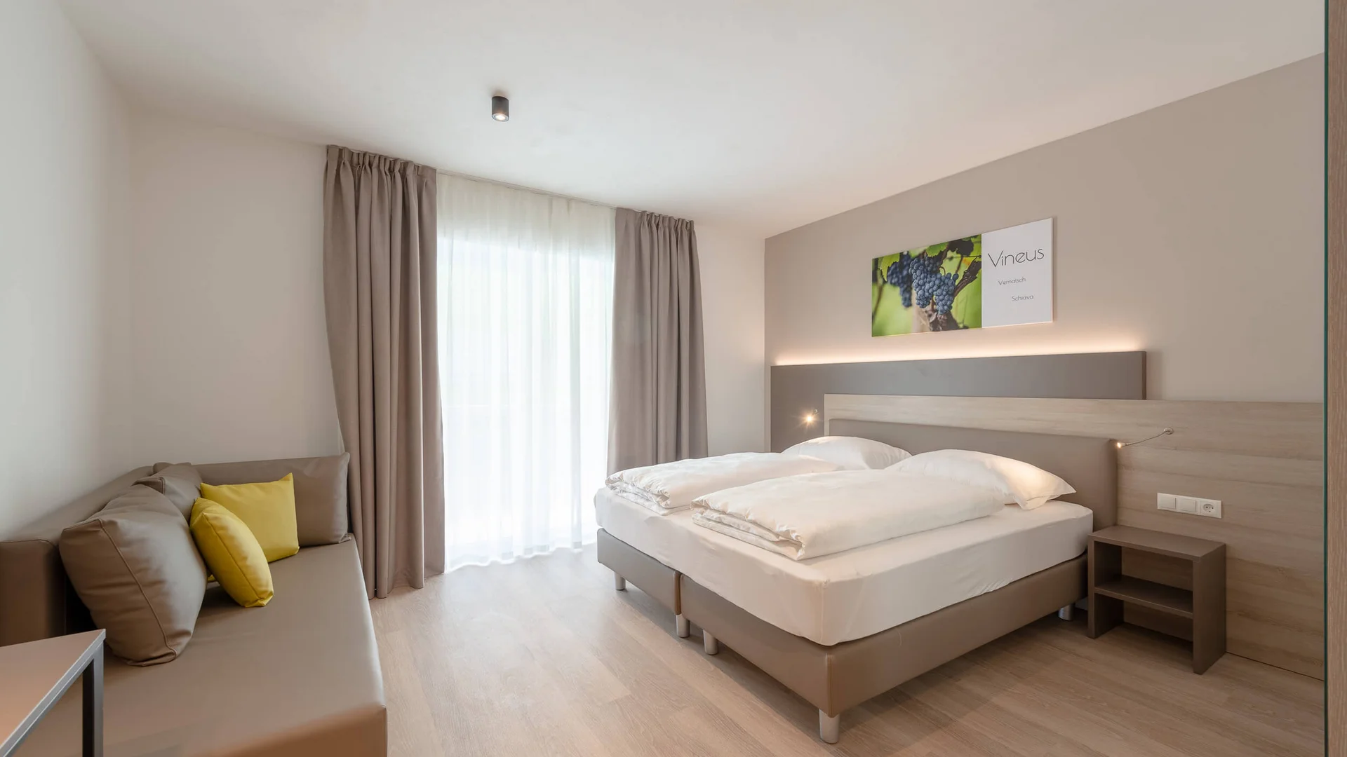 Modernes Hotelzimmer mit zwei Einzelbetten und Sofa neben Fenster