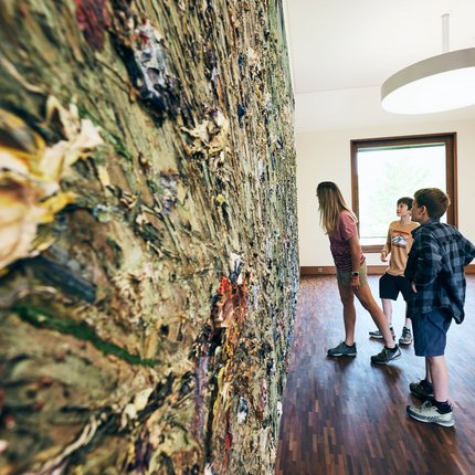 Drie kinderen bekijken een groot abstract schilderij met textuur in een galerij