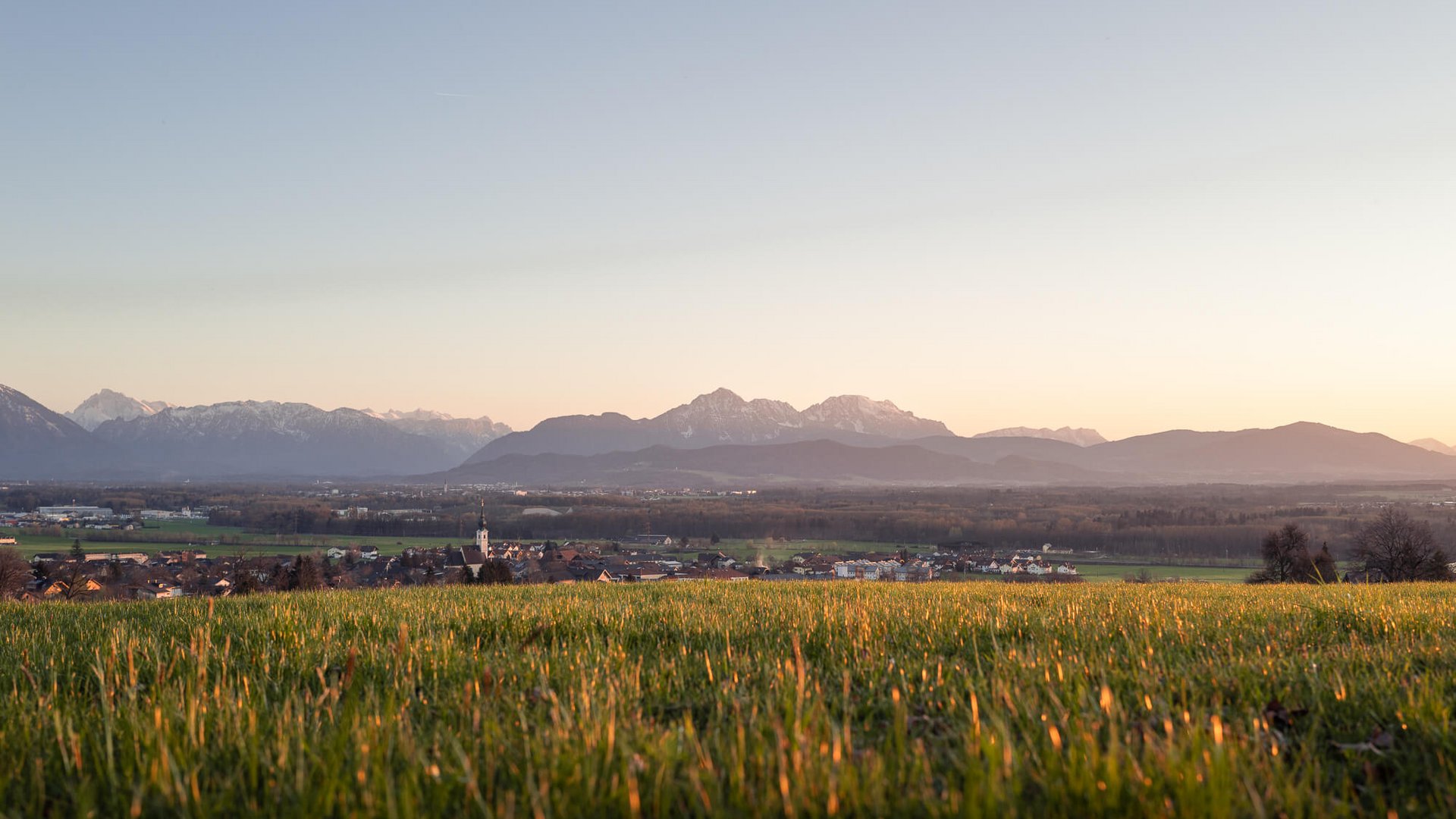 Grünes Feld mit Dorf und Bergpanorama im Sonnenuntergang