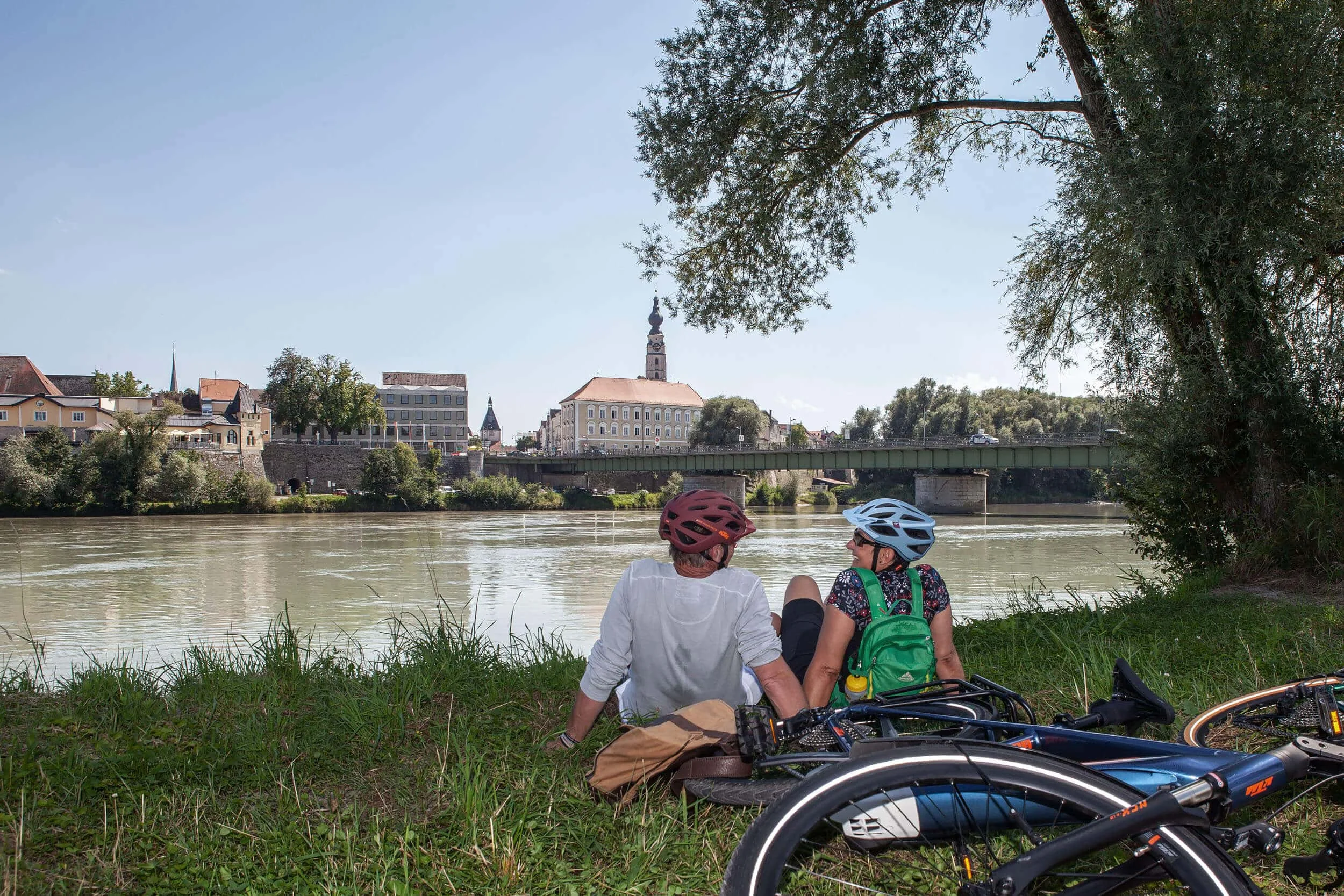 Zwei Radfahrer sitzen am Flussufer mit Blick auf Stadt und Brücke