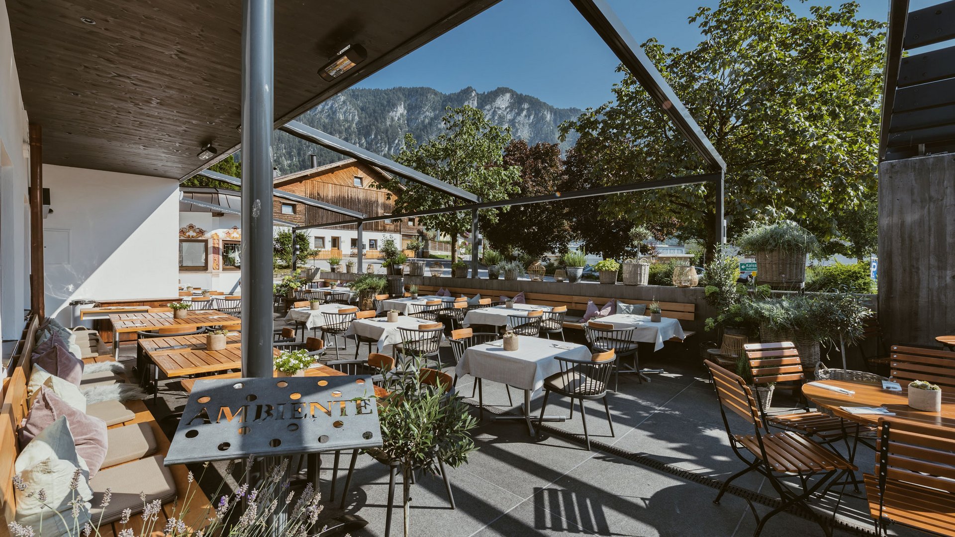 Sonnige Außenrestaurantterrasse mit Tischen, Stühlen und Bergblick