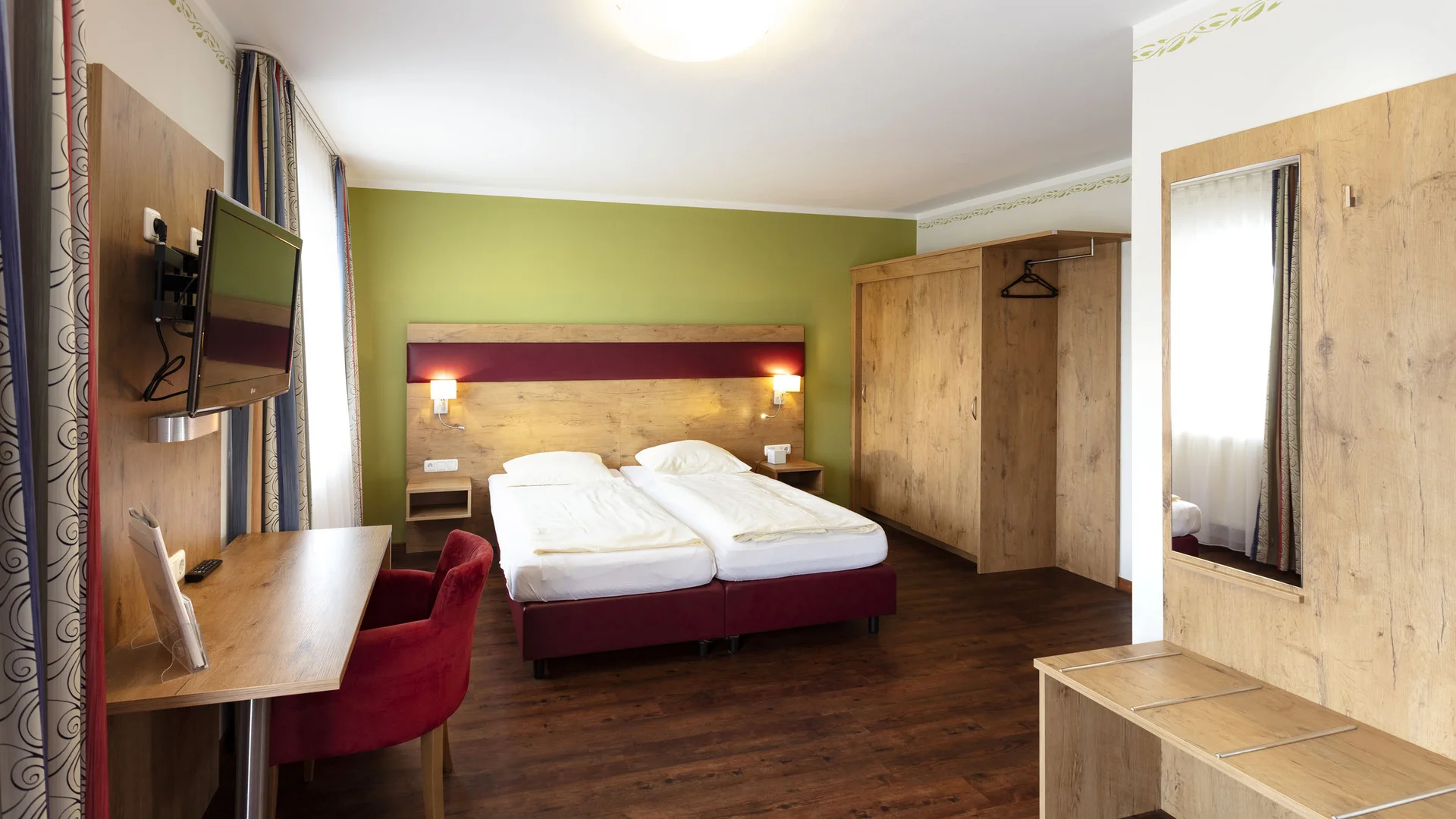 Bright hotel room with double bed, desk, TV, and wooden furniture