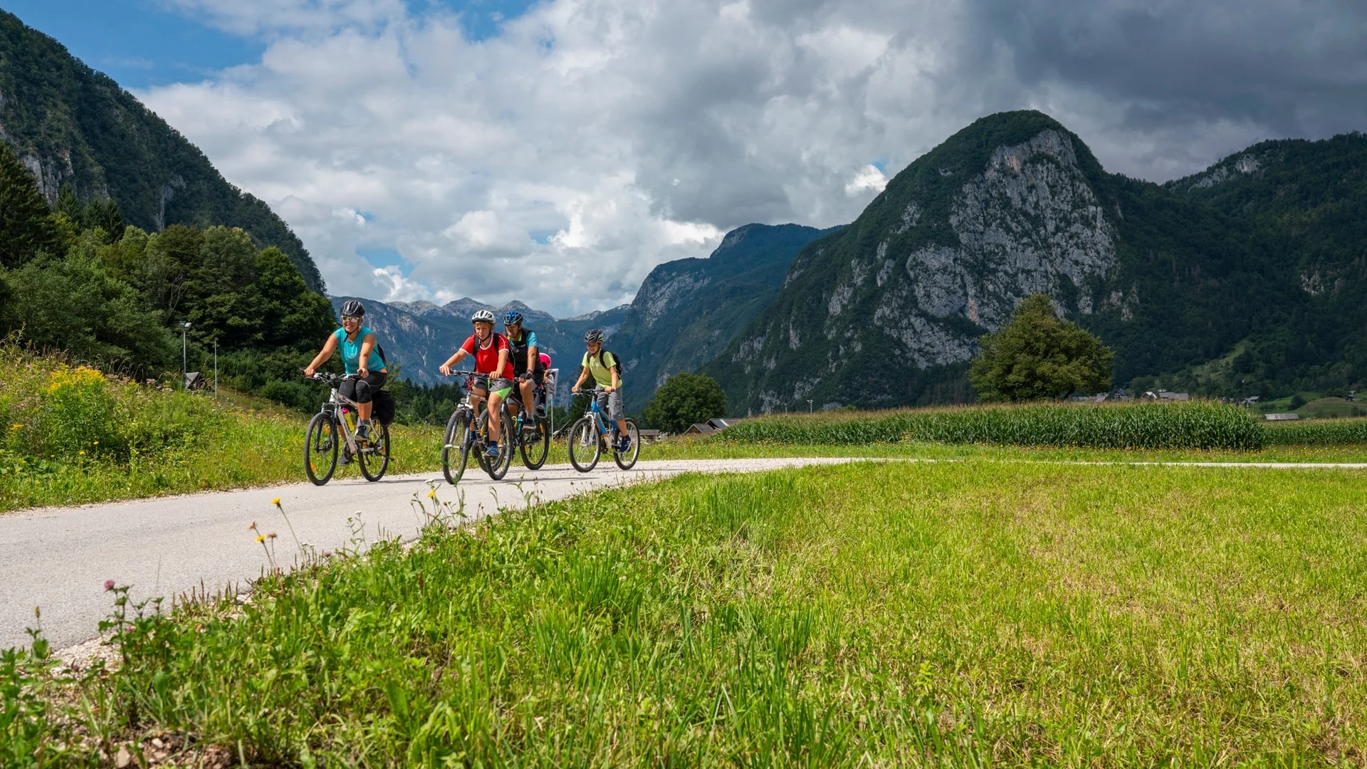 Groep fietsers op landelijke weg in bergachtig landschap onder bewolkte hemel