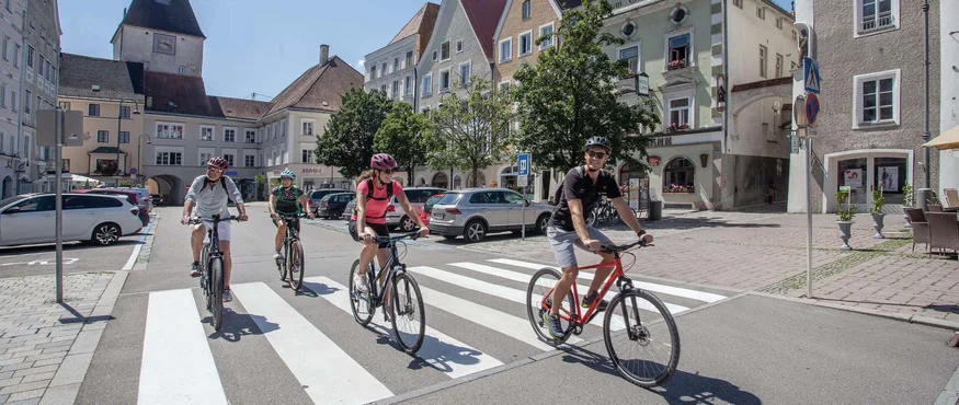 Vier Radfahrer fahren auf einem Zebrastreifen in einer historischen Altstadt bei Sonnenschein