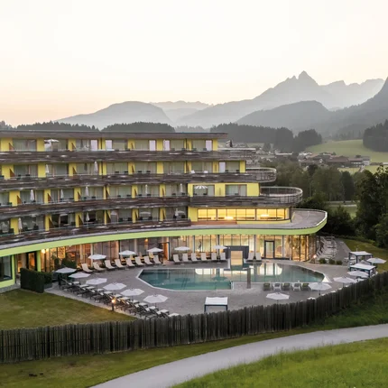 Modernes Hotel mit Pool vor Bergkulisse und Wäldern