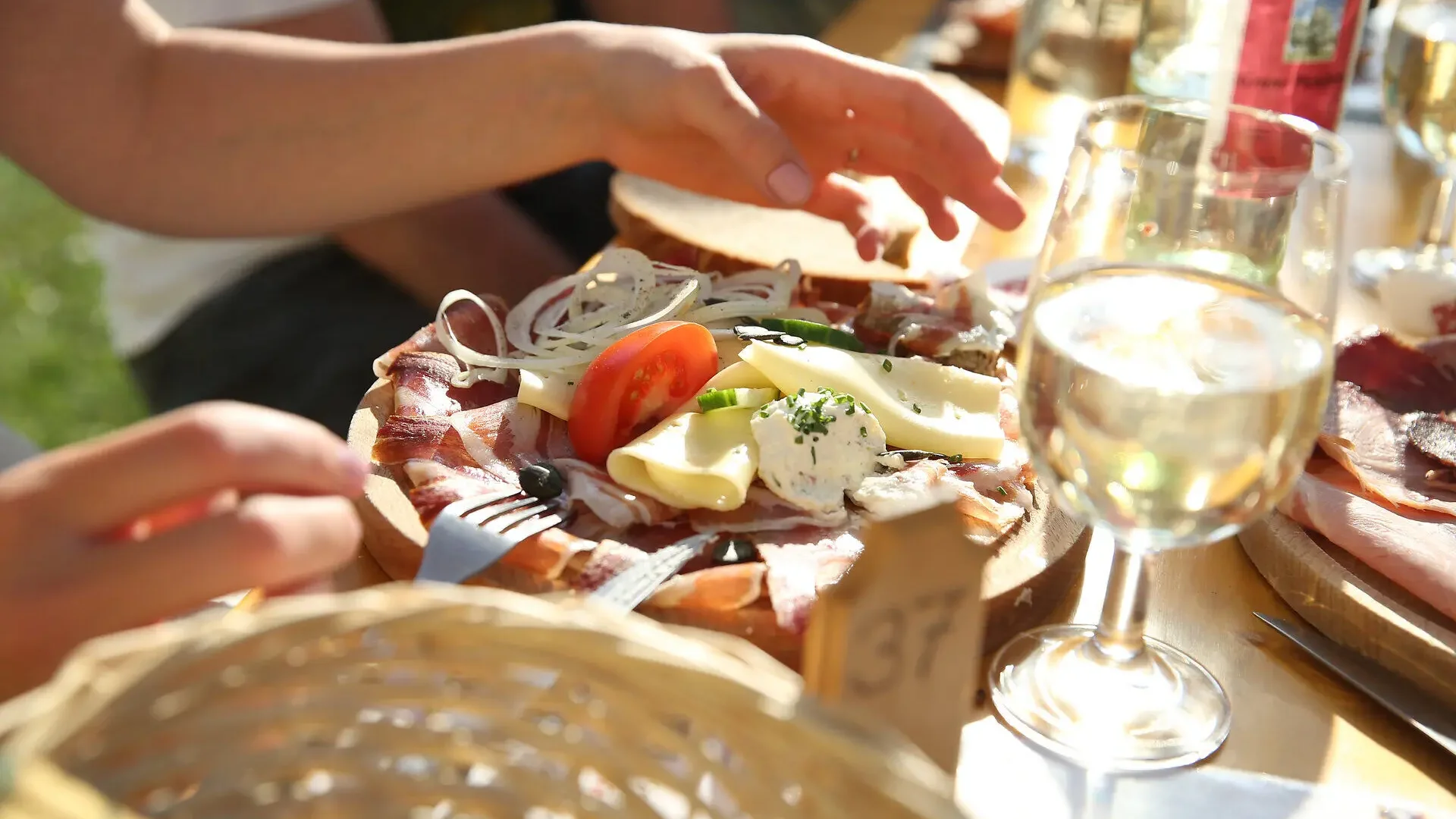 Brotzeitplatte mit Schinken, Käse und Tomaten neben einem Glas Weißwein