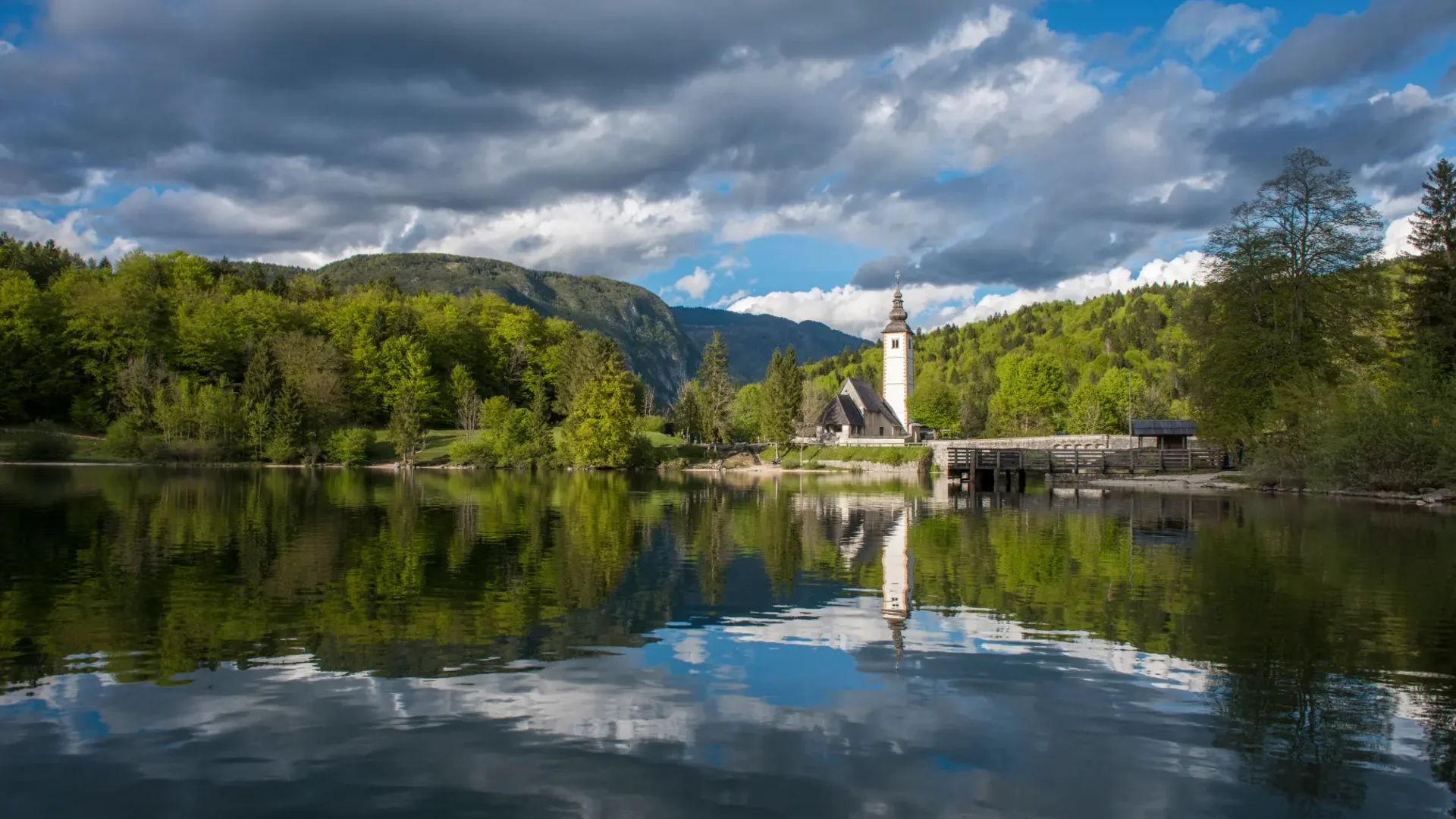 Tour-Detail © Mojca Odar Kirche am See mit Bergkulisse und dramatischem Wolkenhimmel