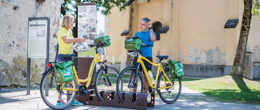Two people with yellow rental bikes at an outdoor information board