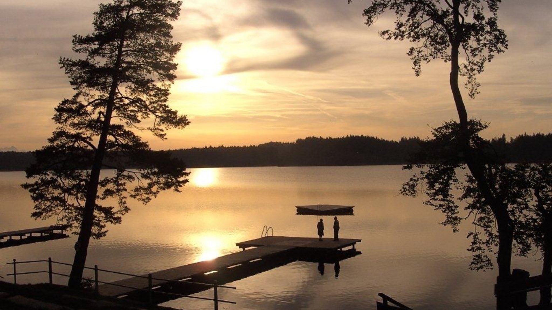 Sunset over calm lake with pier and two people standing