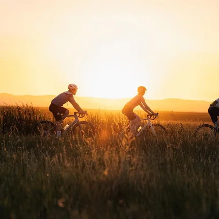 Drei Radfahrer fahren bei Sonnenuntergang durch hohes Gras
