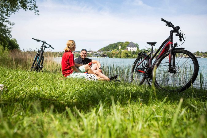 Zwei Radfahrer entspannen am Seeufer mit ihren Fahrrädern im Gras