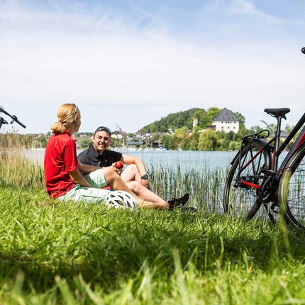 Two cyclists resting on lake shore with their bikes on grass