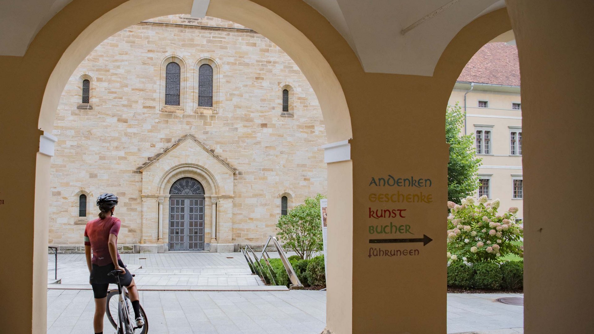 Person with bicycle under an archway near a historic building