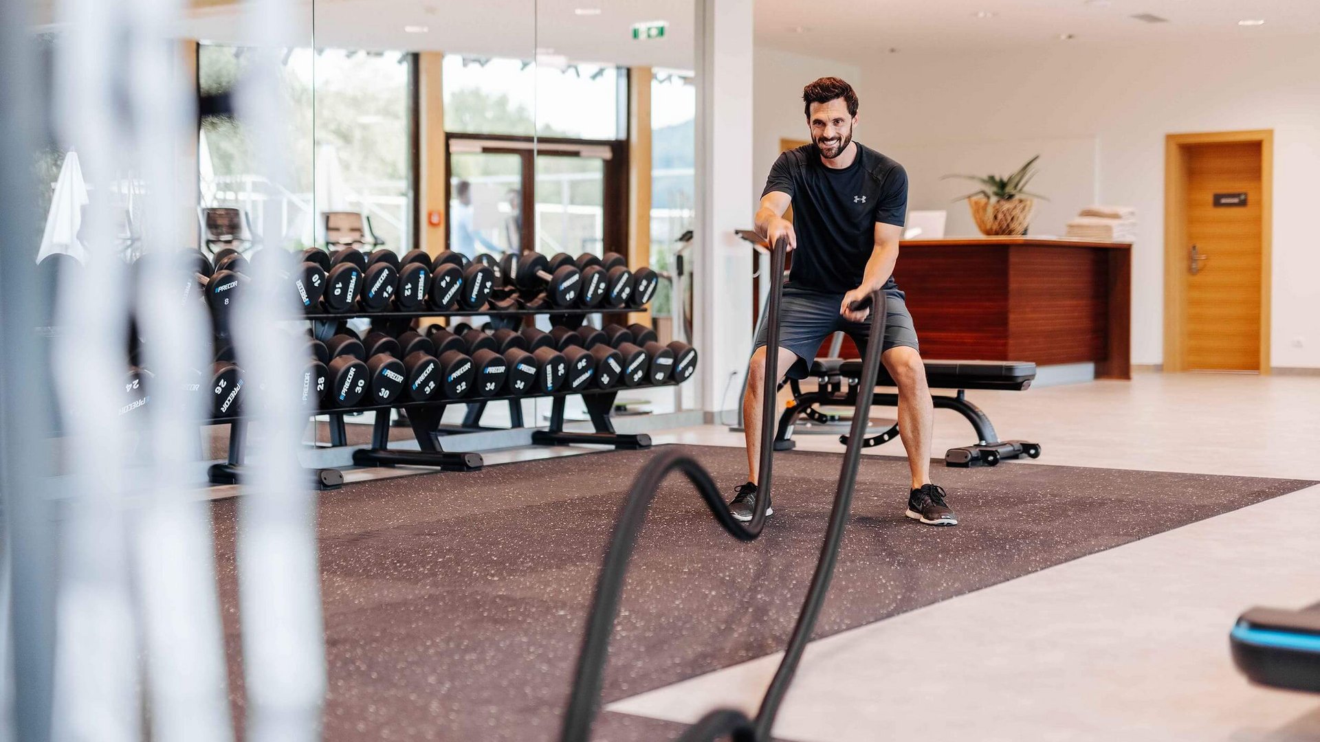Man exercising with battle ropes in gym with dumbbells in background