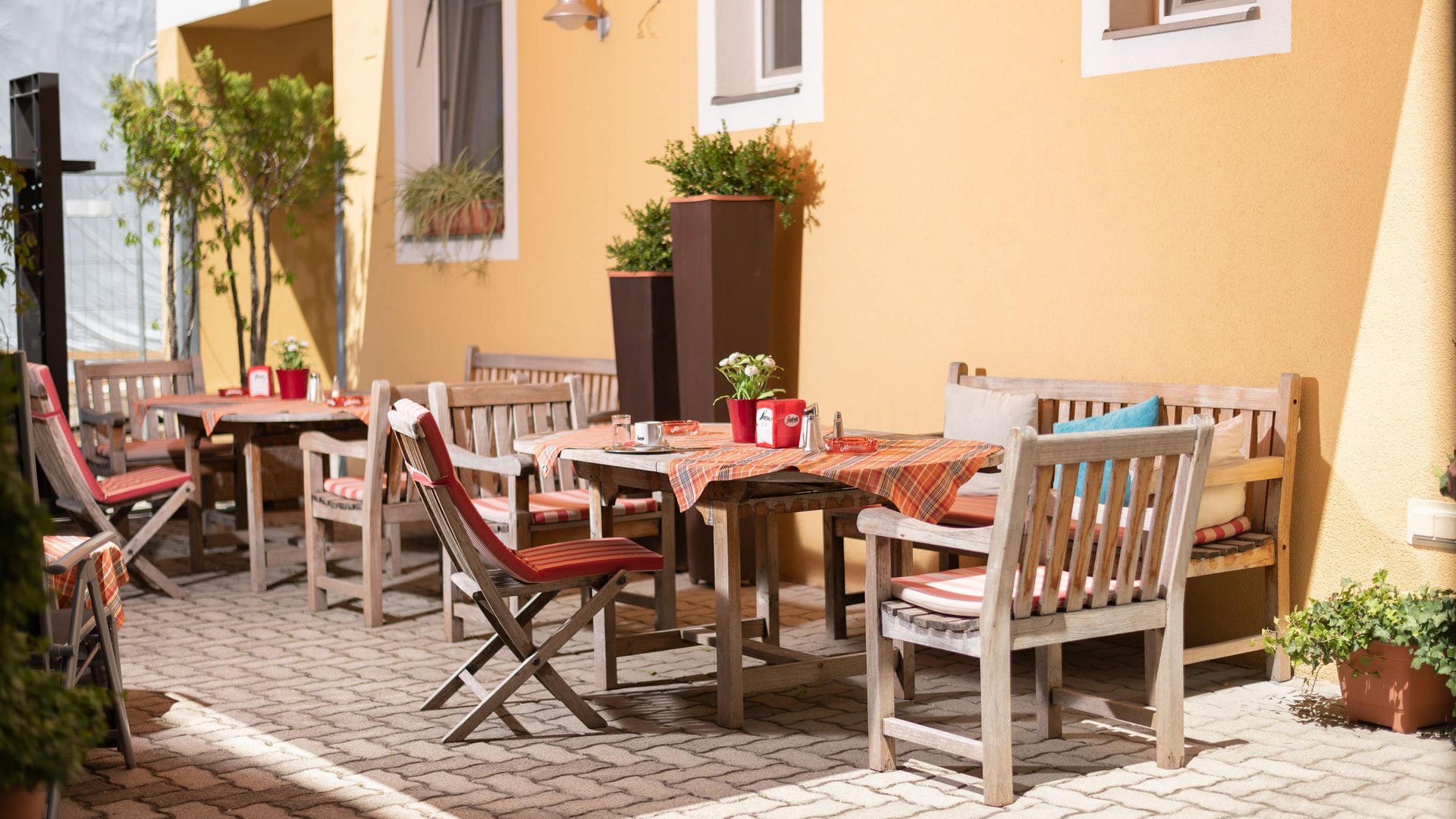 Sunny outdoor patio with wooden tables and chairs by yellow wall