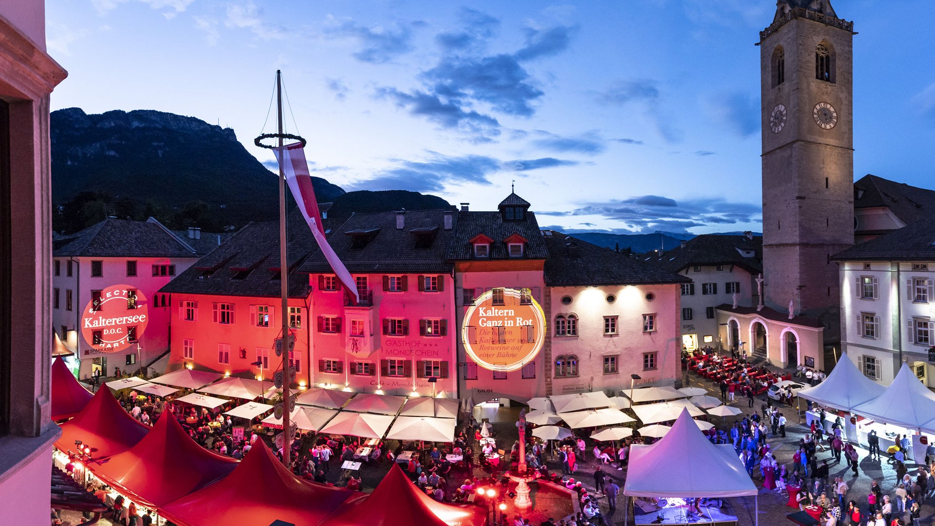 Festival with red tents and lit buildings in a historic square at dusk