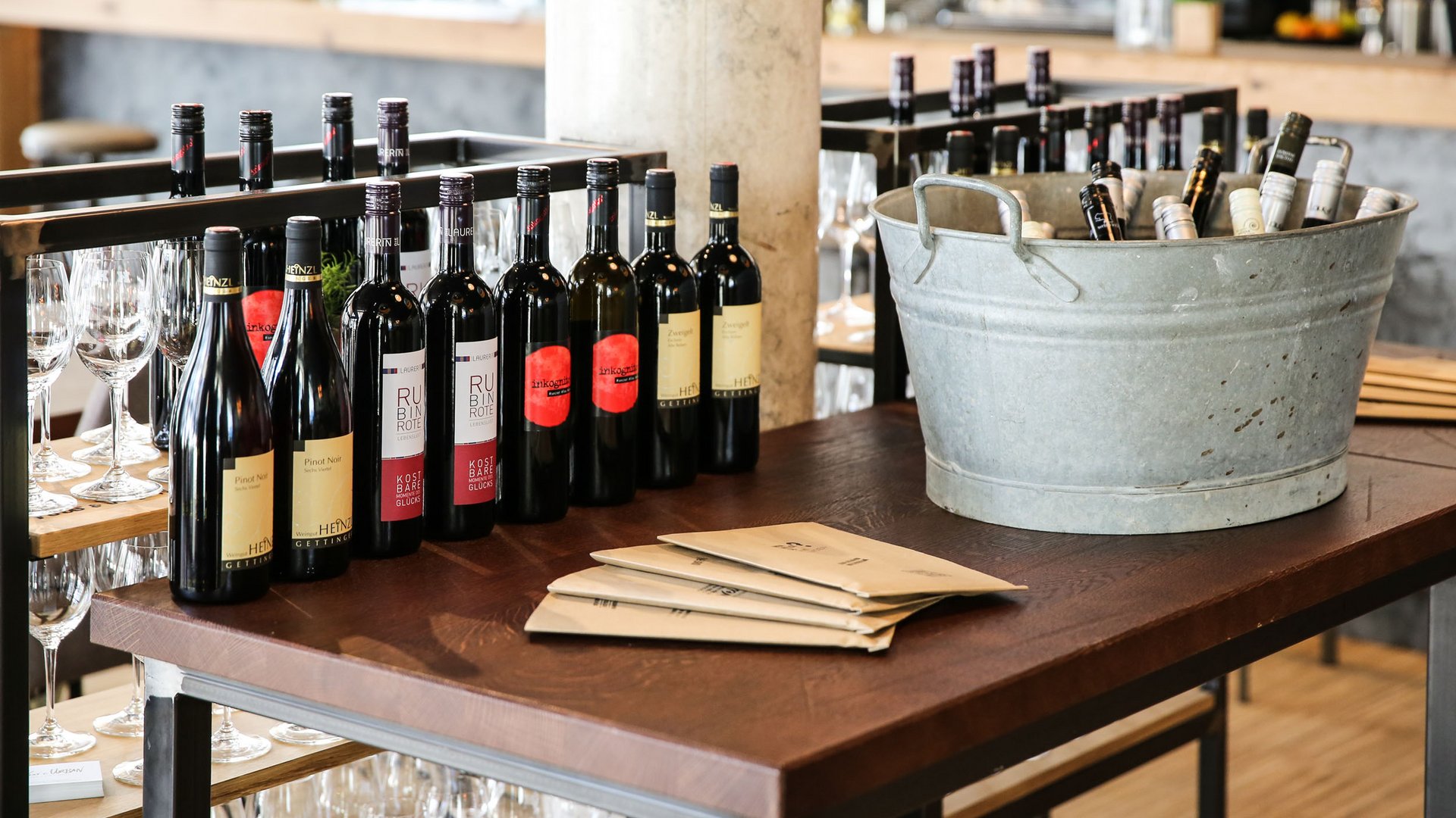Multiple wine bottles and a metal bucket on a wooden table in a restaurant