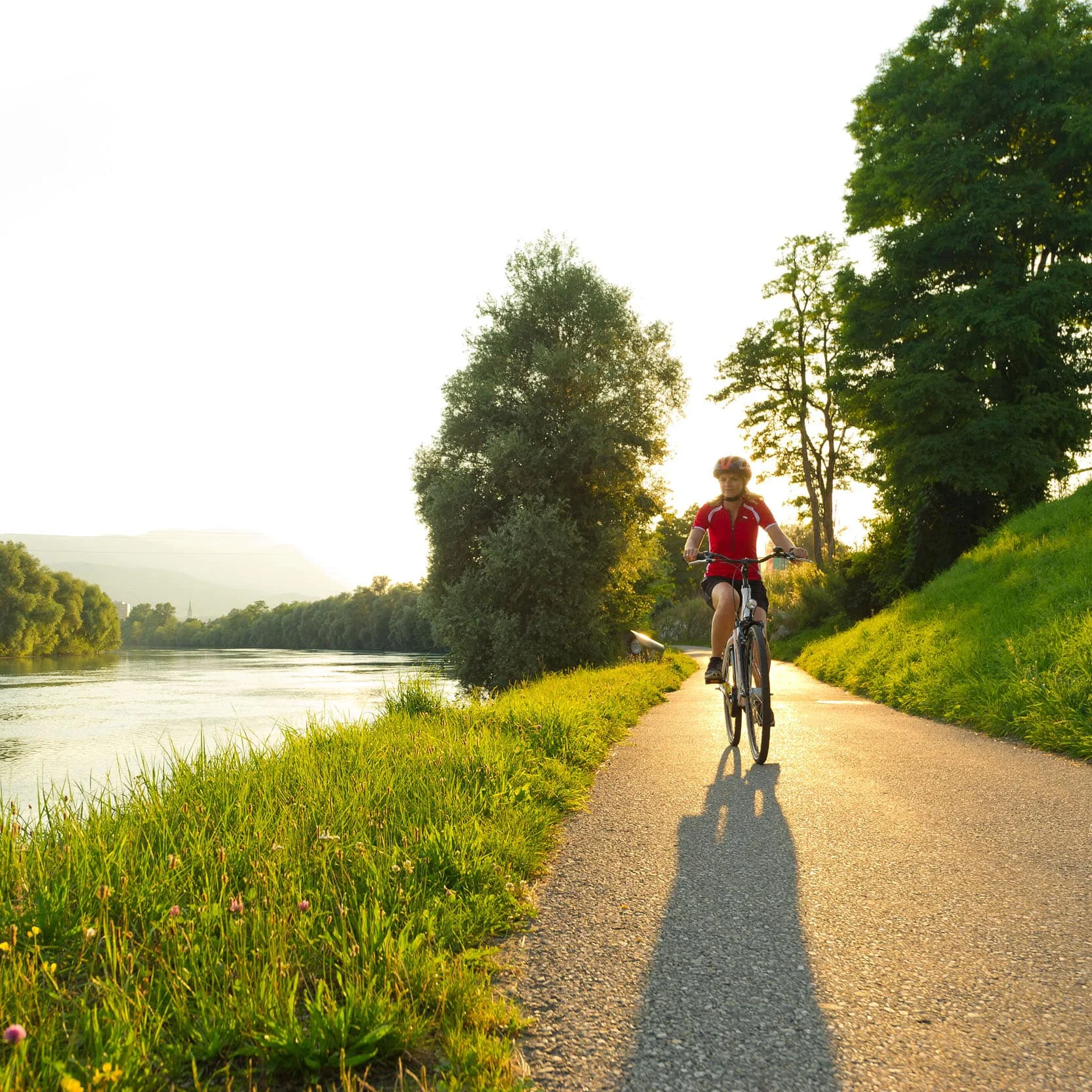 Fahrradfahrer fährt am Fluss entlang auf einem sonnigen Radweg