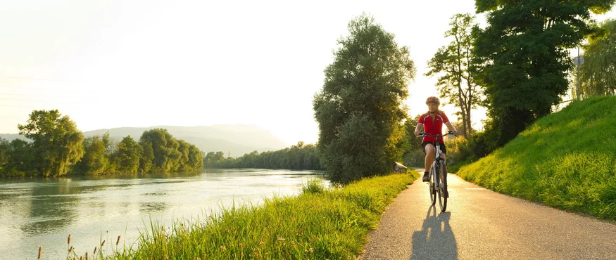 Fahrradfahrer fährt am Fluss entlang auf einem sonnigen Radweg