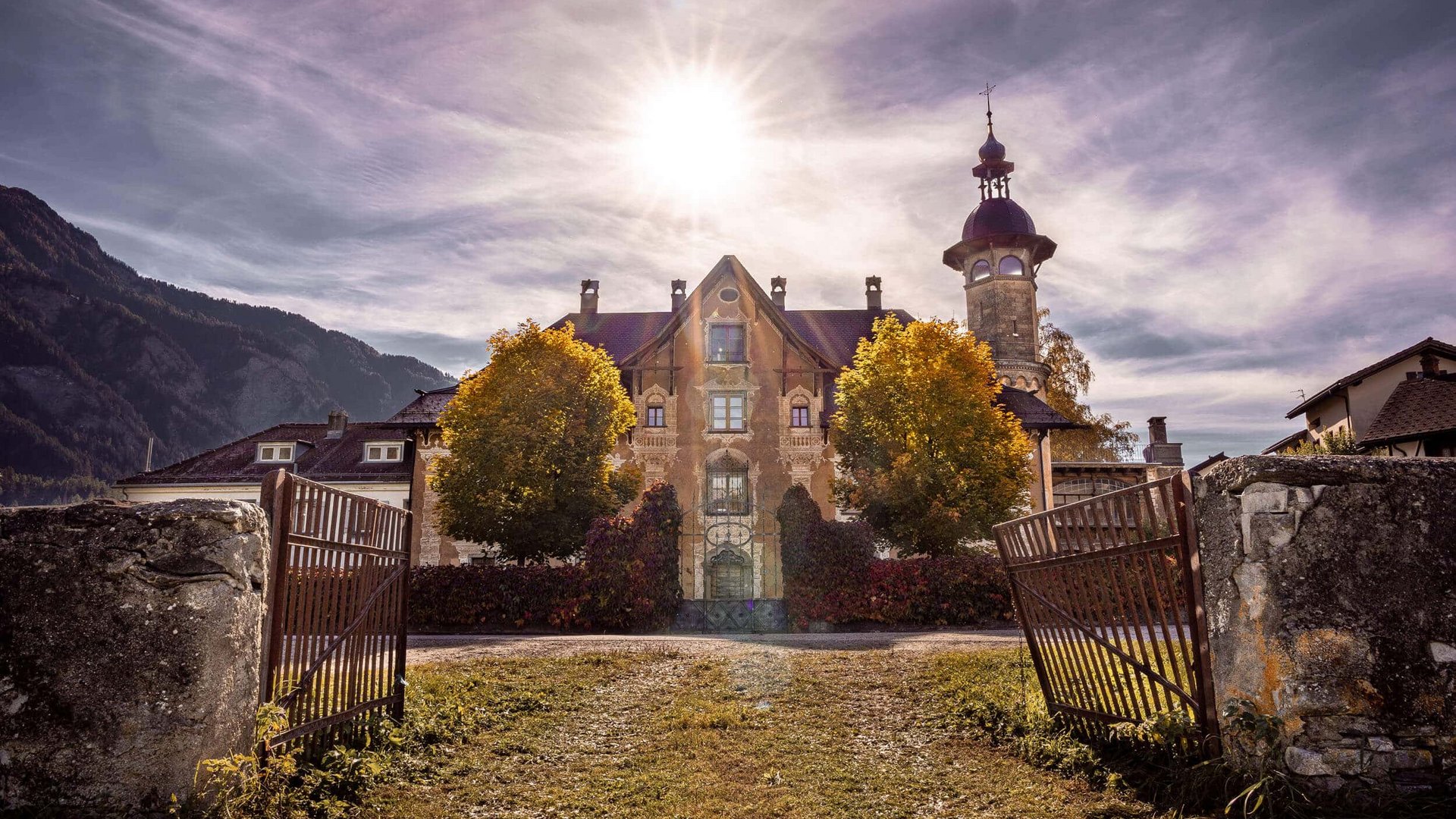 Historic building with open gate and mountains in the background under bright sun