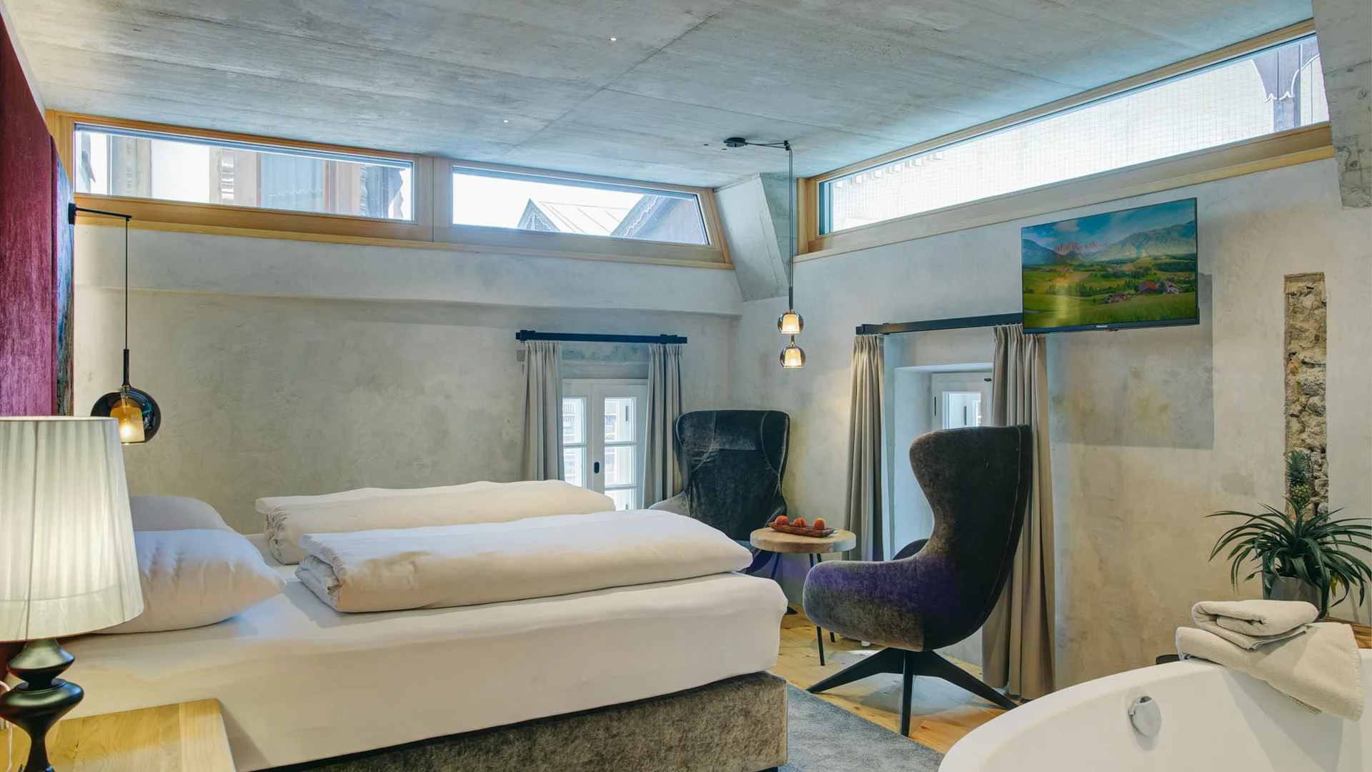 Modern hotel room with bed, armchairs, and a freestanding bathtub