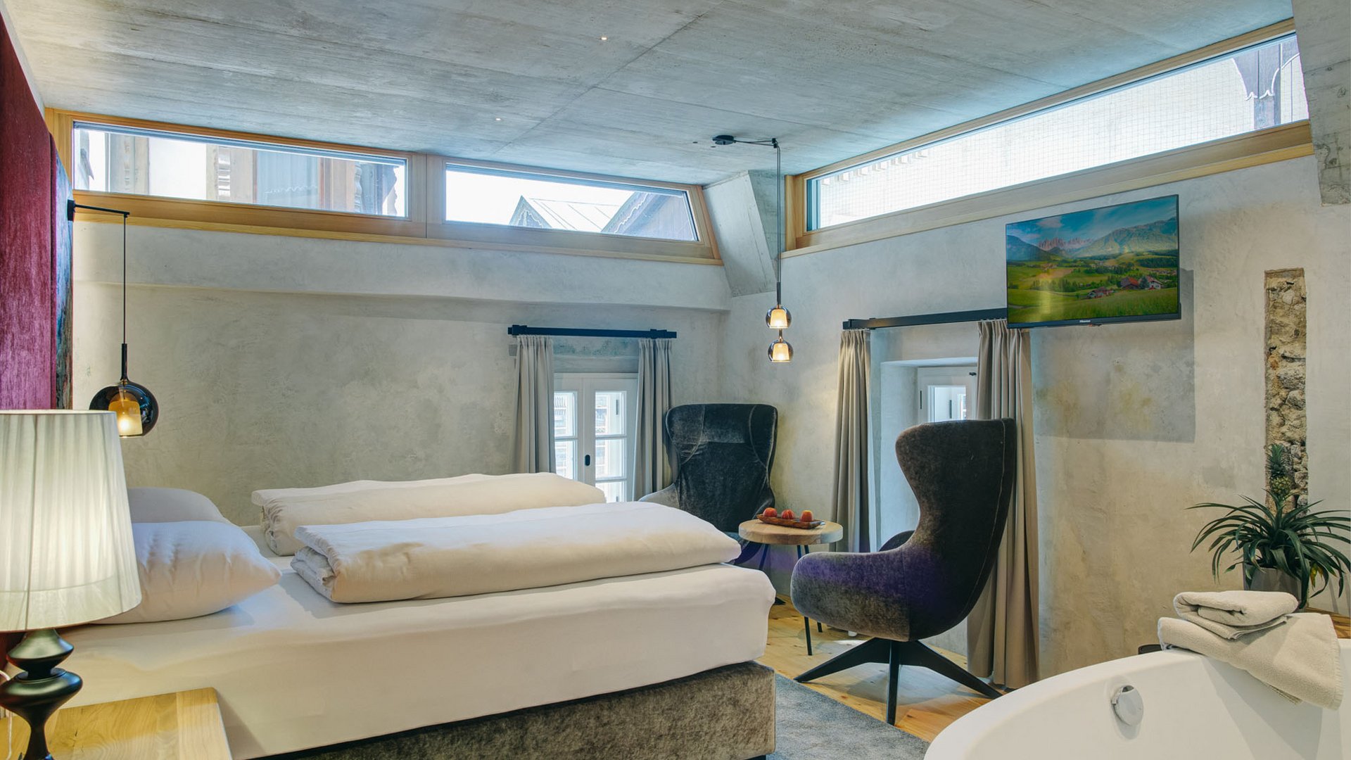 Modern hotel room with bed, armchairs, and a freestanding bathtub