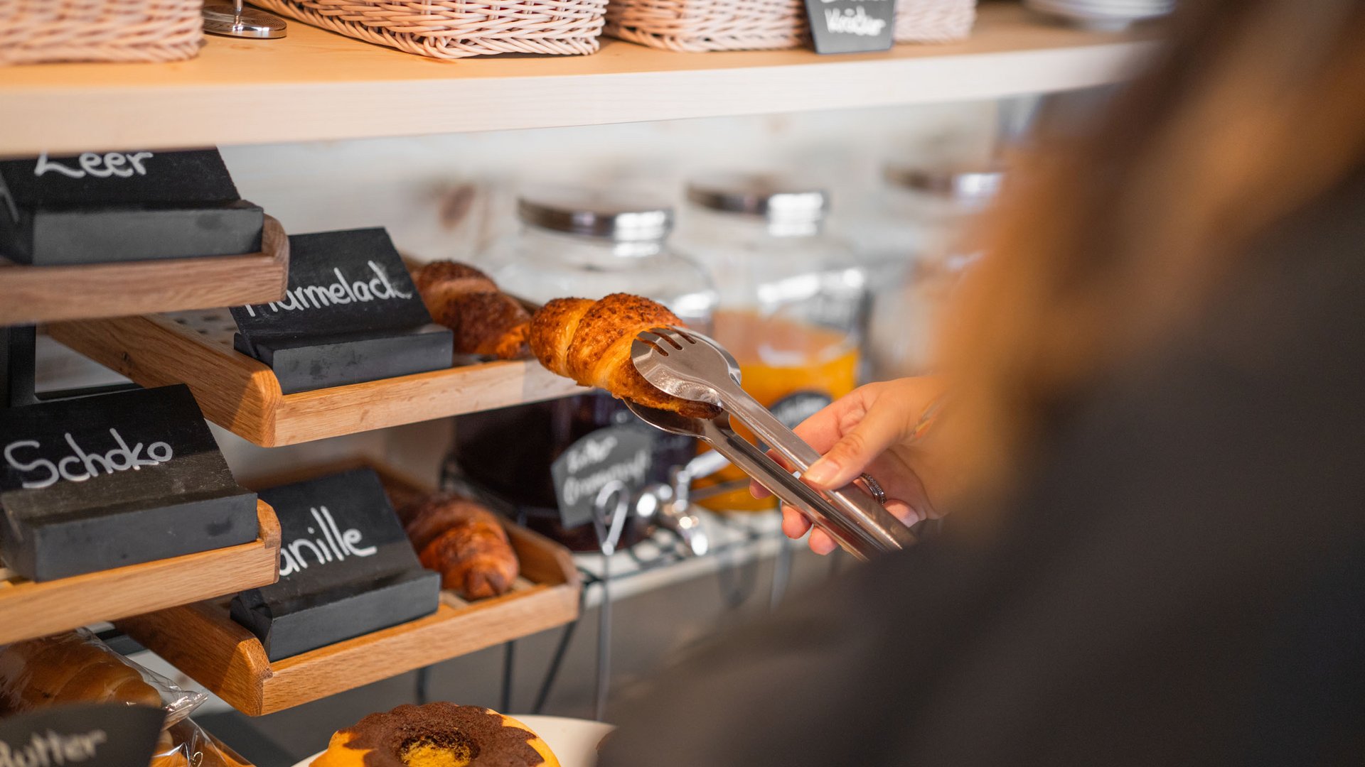 Person using tongs to take a croissant from a shelf