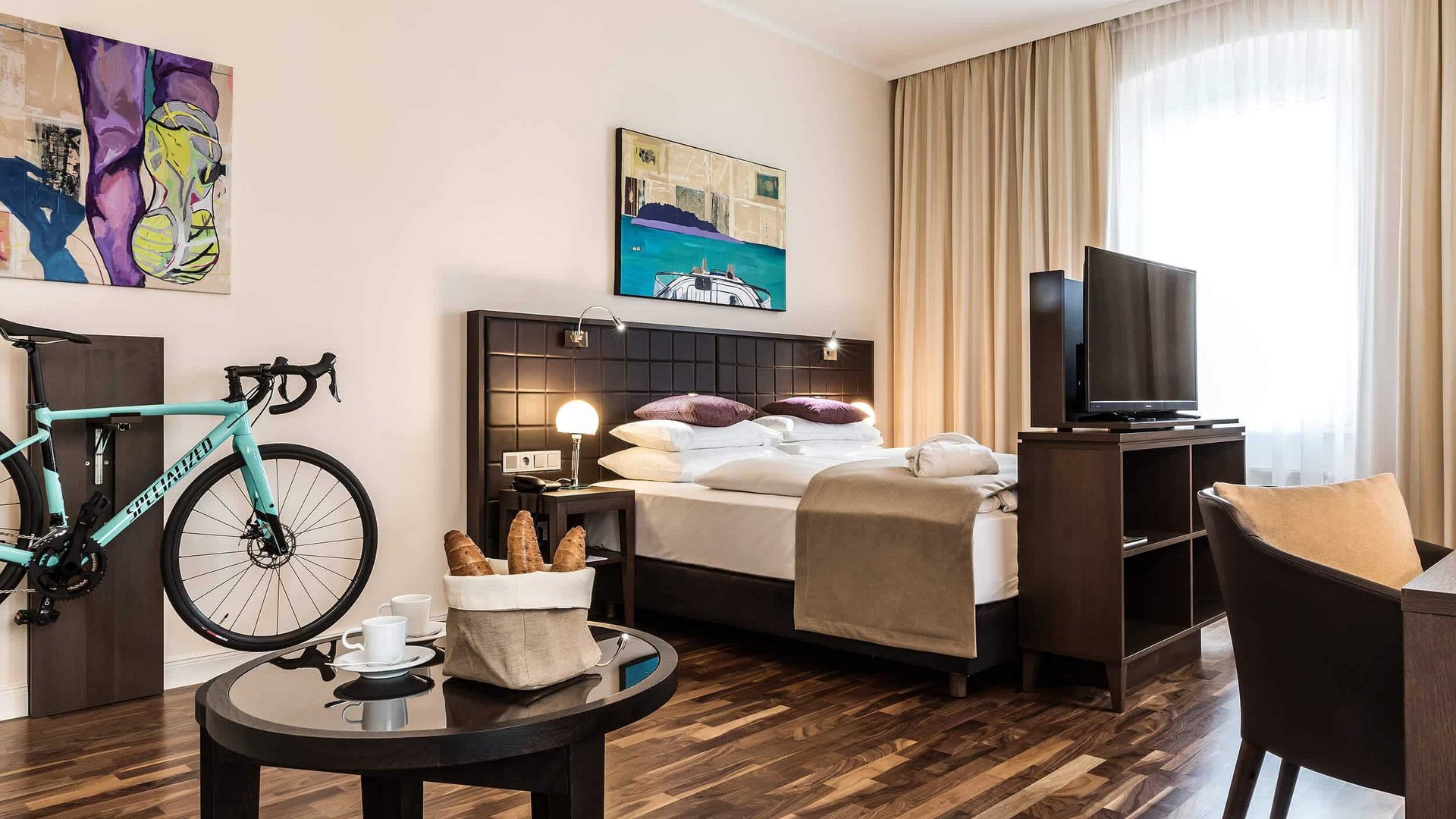 Modern hotel room with double bed, bike on wall, and breakfast table