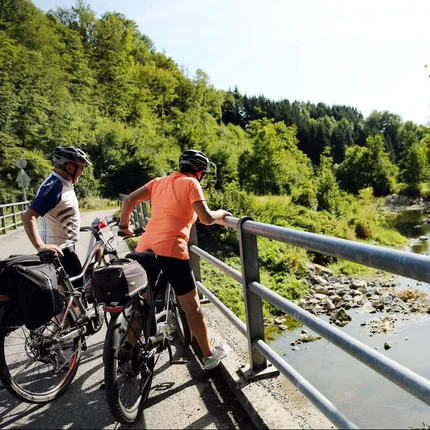 Twee fietsers kijken vanaf een brug naar een rivier in groen landschap